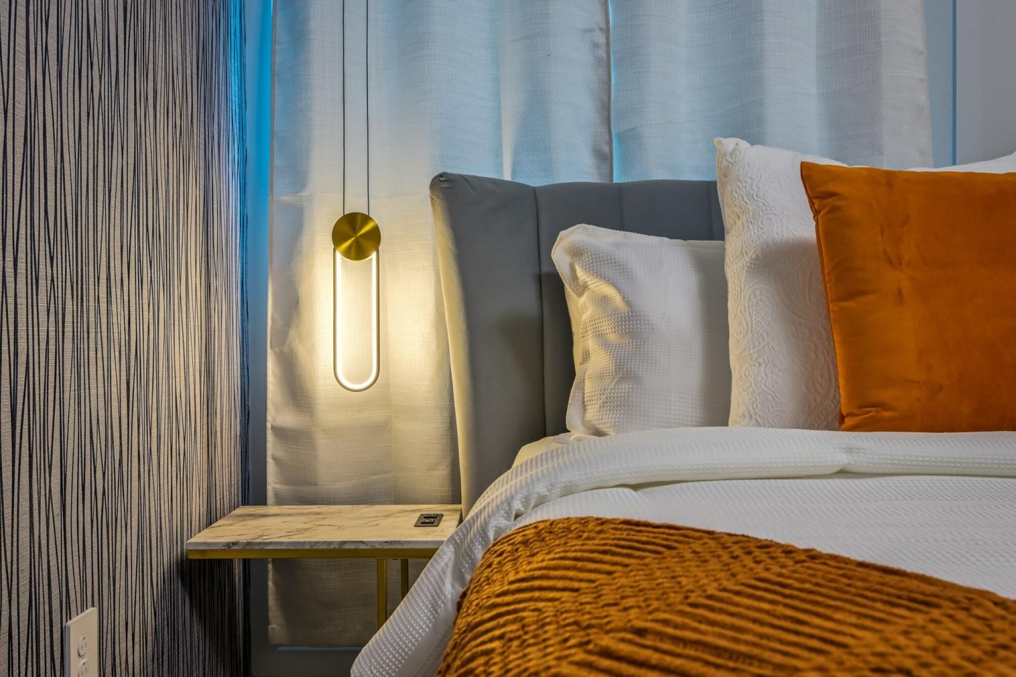 Een moderne hotelkamer met een bed, nachtkastje en een wandlamp.