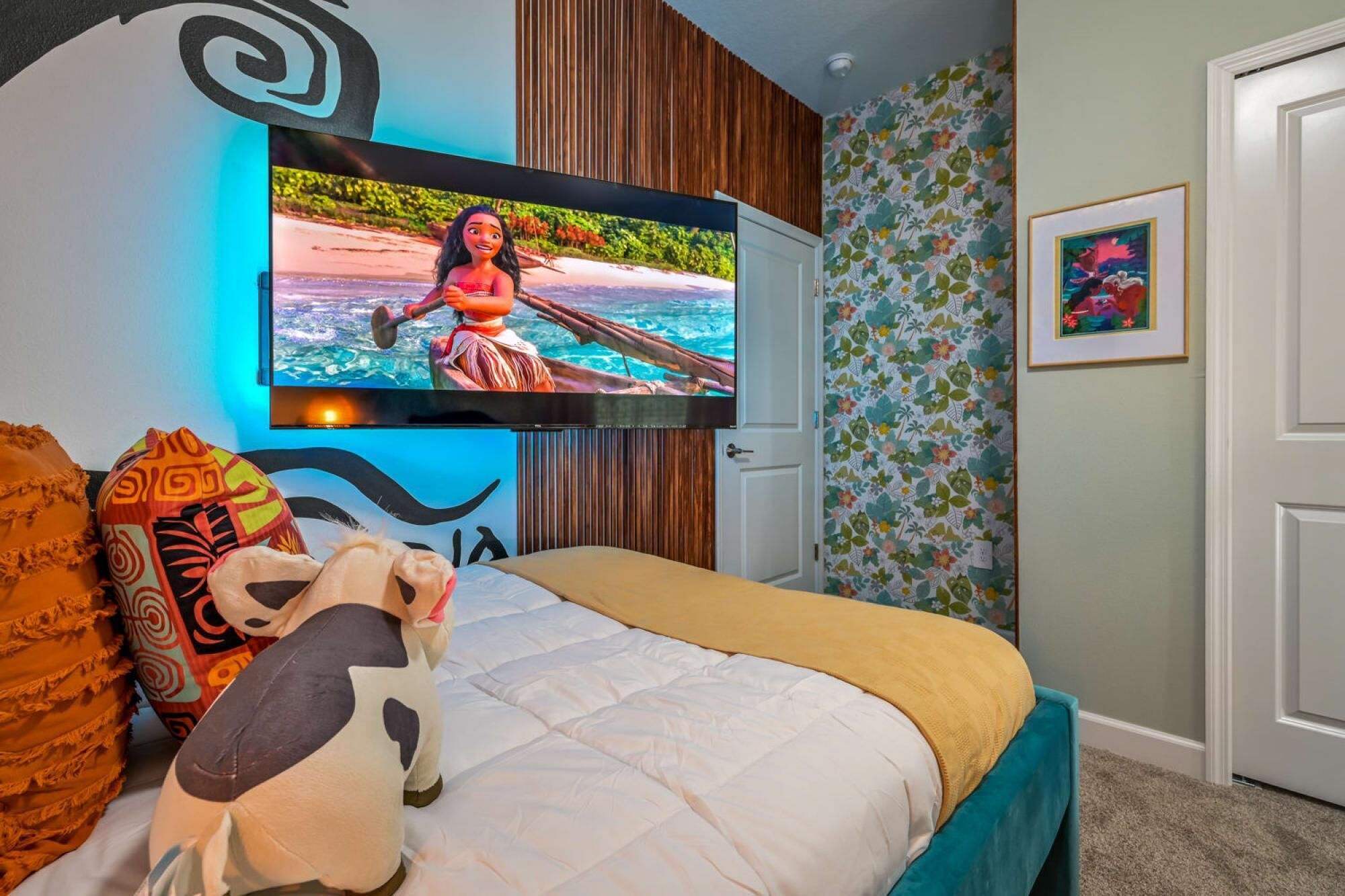Ein Schlafzimmer mit einem Bett, einem an der Wand montierten Fernseher, einem Kuscheltier und einem gerahmten Bild.