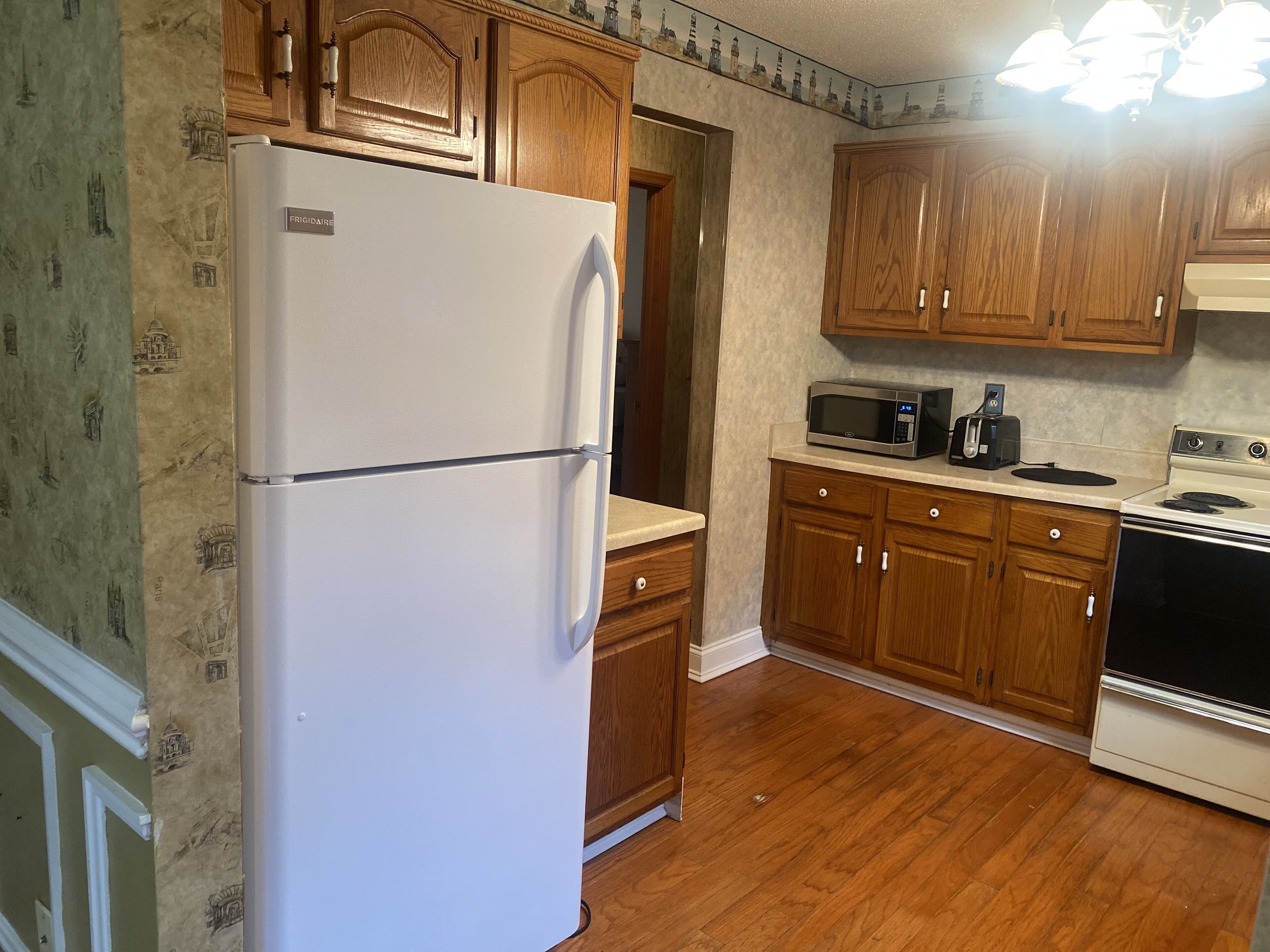 A kitchen with wooden cabinets, a white refrigerator, a microwave, a toaster, and a stove.