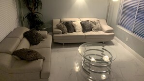 Een woonkamer met een beige bank, een glazen salontafel en een plant in pot.