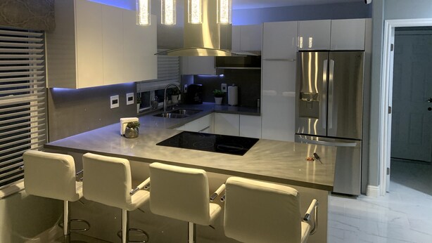 Een moderne keuken met een centraal eiland, roestvrijstalen apparatuur, hangende lampen en barstoelen.