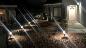 Een oprit met grind, een pad dat naar een huis leidt, en een rij buitenverlichting langs het pad.