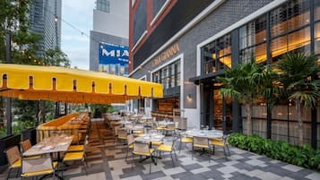 An outdoor dining area with yellow umbrellas, tables, and chairs arranged in a linear fashion.