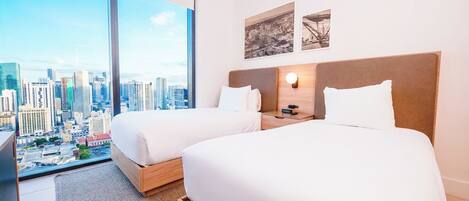 A hotel room with two beds, a large window with a city view, and a nightstand with a lamp.