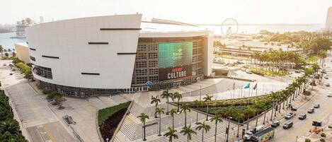 A modern building with a large digital display, surrounded by palm trees and a waterfront.