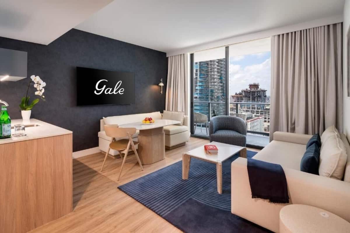A modern hotel room with a city view, a dining area, and a living space.