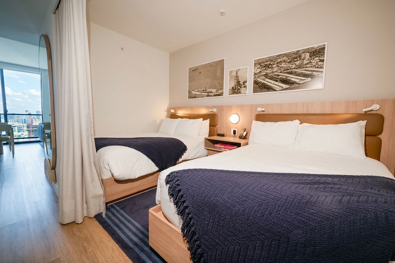 Habitación de hotel con dos camas, un ventanal grande y vistas a la ciudad.