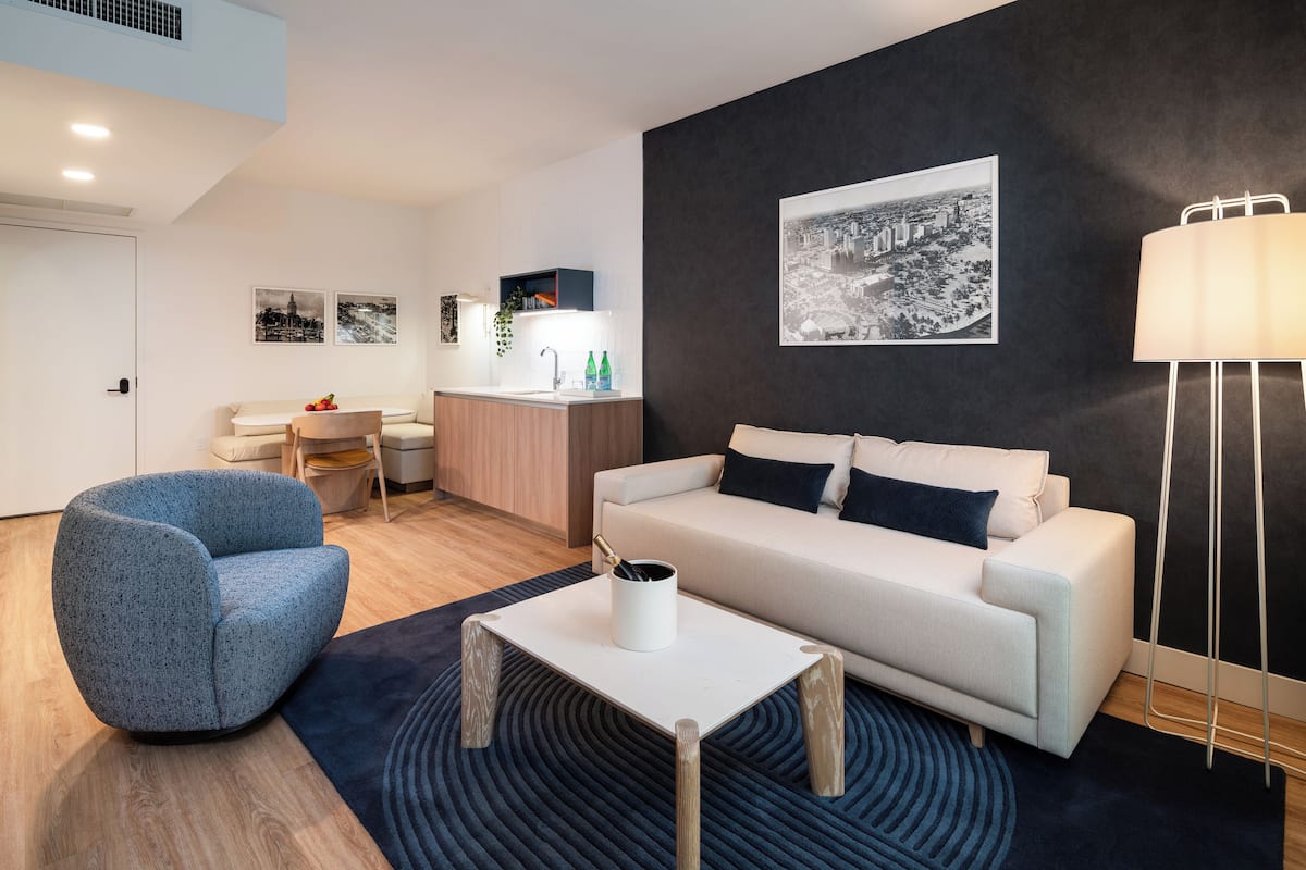 A modern living room with a sofa, a blue armchair, a coffee table, and a black and white cityscape painting on the wall.