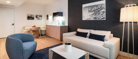 A modern living room with a sofa, a blue armchair, a coffee table, and a black and white cityscape painting on the wall.