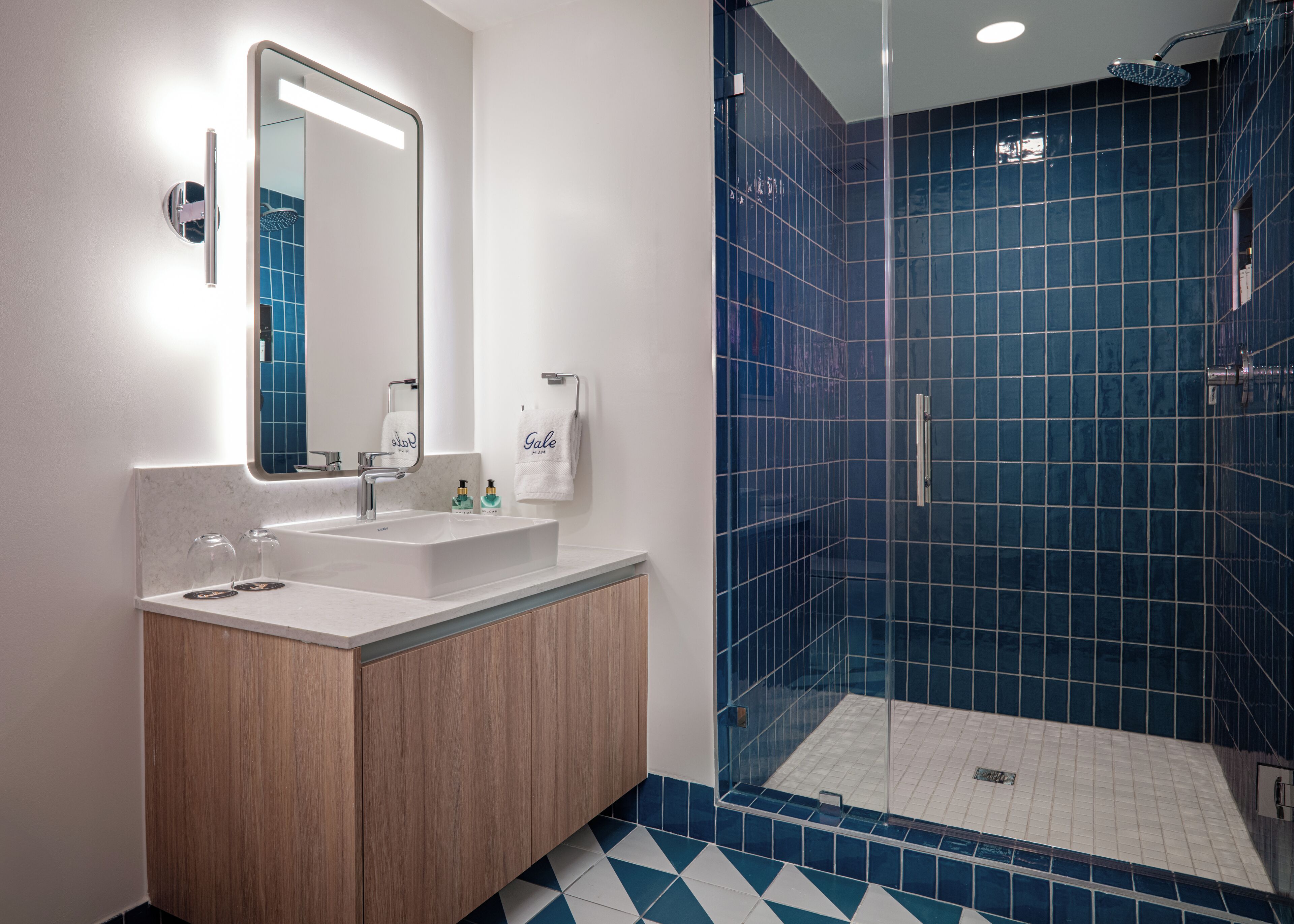 A modern bathroom with a large mirror, a sink, and a shower area with blue tiles.