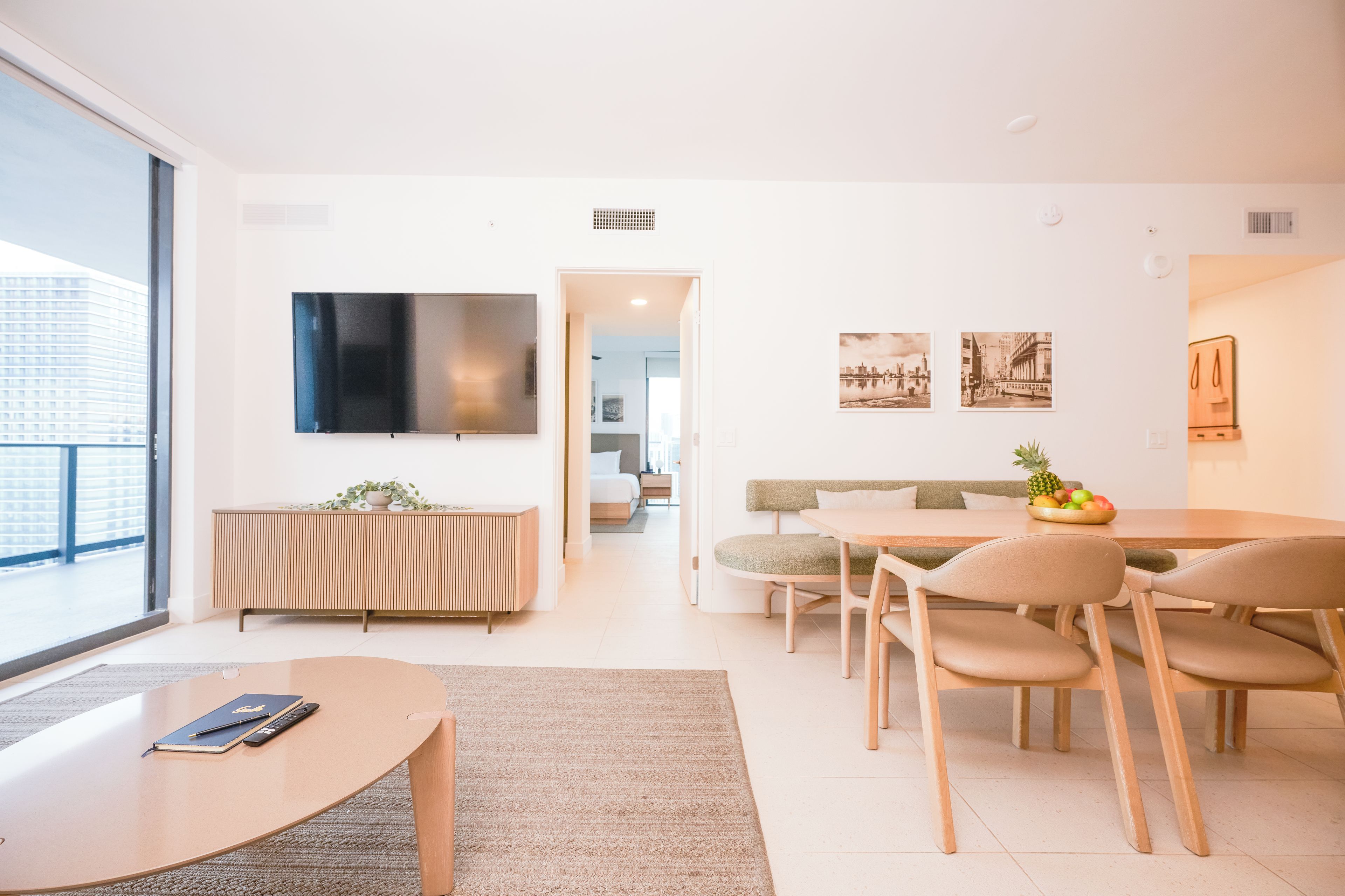 A modern living room with a flat-screen TV, a sofa, a dining table with chairs, and a coffee table.