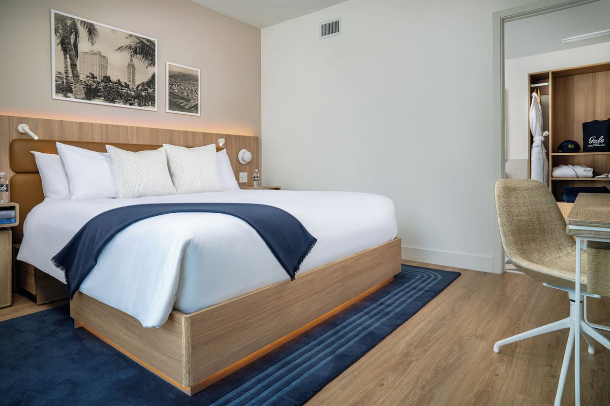 A hotel room with a large bed, a desk with a chair, and a wardrobe.