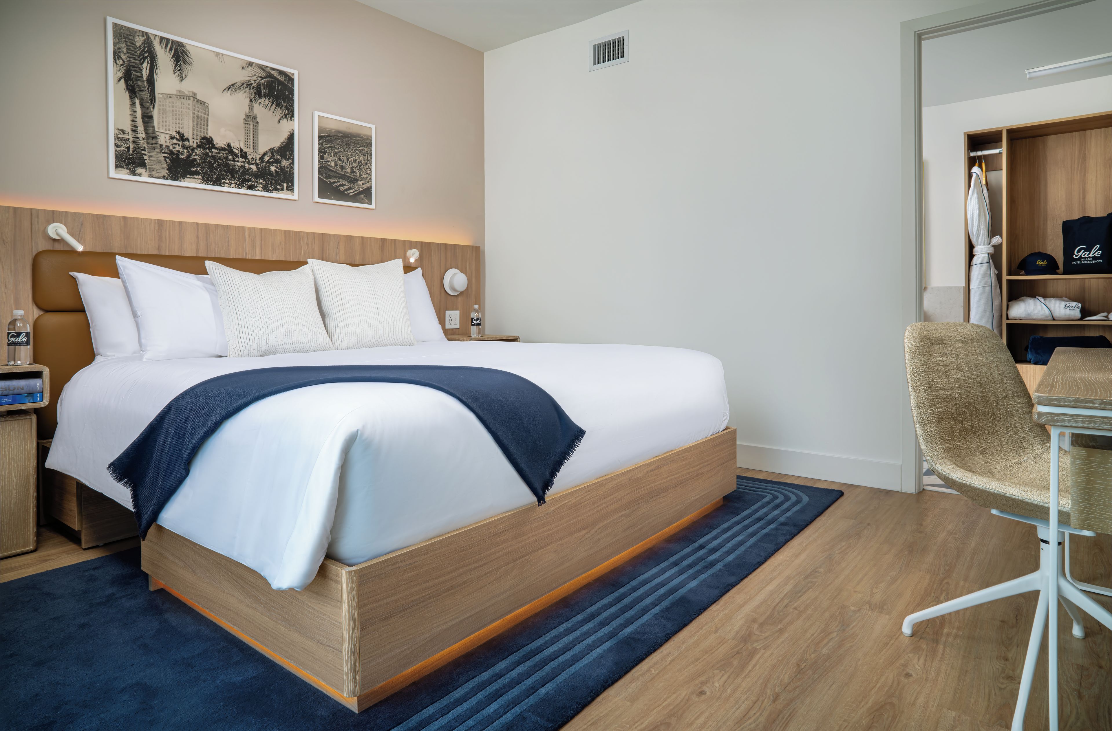 A hotel room with a large bed, a desk with a chair, and a wardrobe.