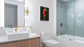 A modern bathroom with a white sink, gold fixtures, a toilet, and a glass-enclosed shower.