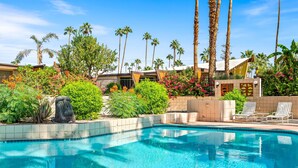 A swimming pool with lounge chairs, surrounded by palm trees and various plants.