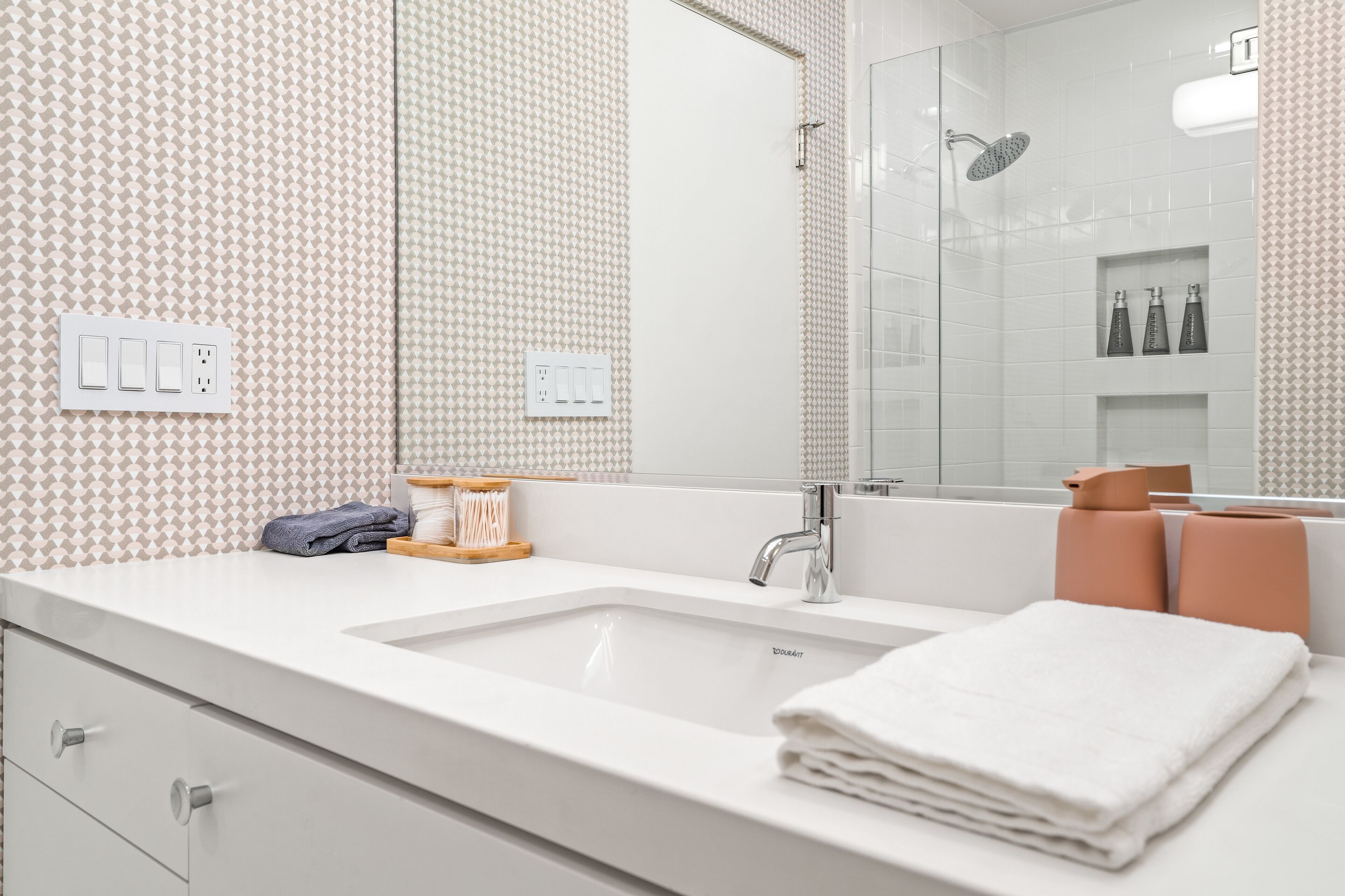 A modern bathroom with a large mirror, white sink, and a shower area.