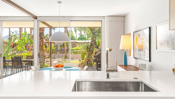 A modern kitchen with a large island, a dining area with outdoor seating, and a view of a garden and pool.