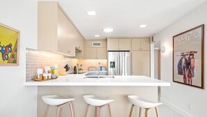 A modern kitchen with a white island, stainless steel appliances, and three white bar stools.