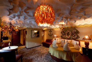 A room with a unique ceiling design, a bed with decorative pillows, and a wall-mounted lamp.