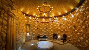 Una habitación con paredes de piedra, una bañera grande, un sofá negro y un candelabro.