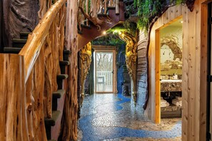 Una escala de fusta amb un disseny natural que recorda a un arbre, que condueix a una habitació amb una paret de pedra i una porta.