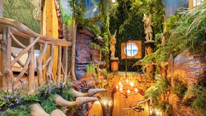 Un interior con temática de bosque, que incluye un puente de madera, una estatua y una pared con un ventanal circular.