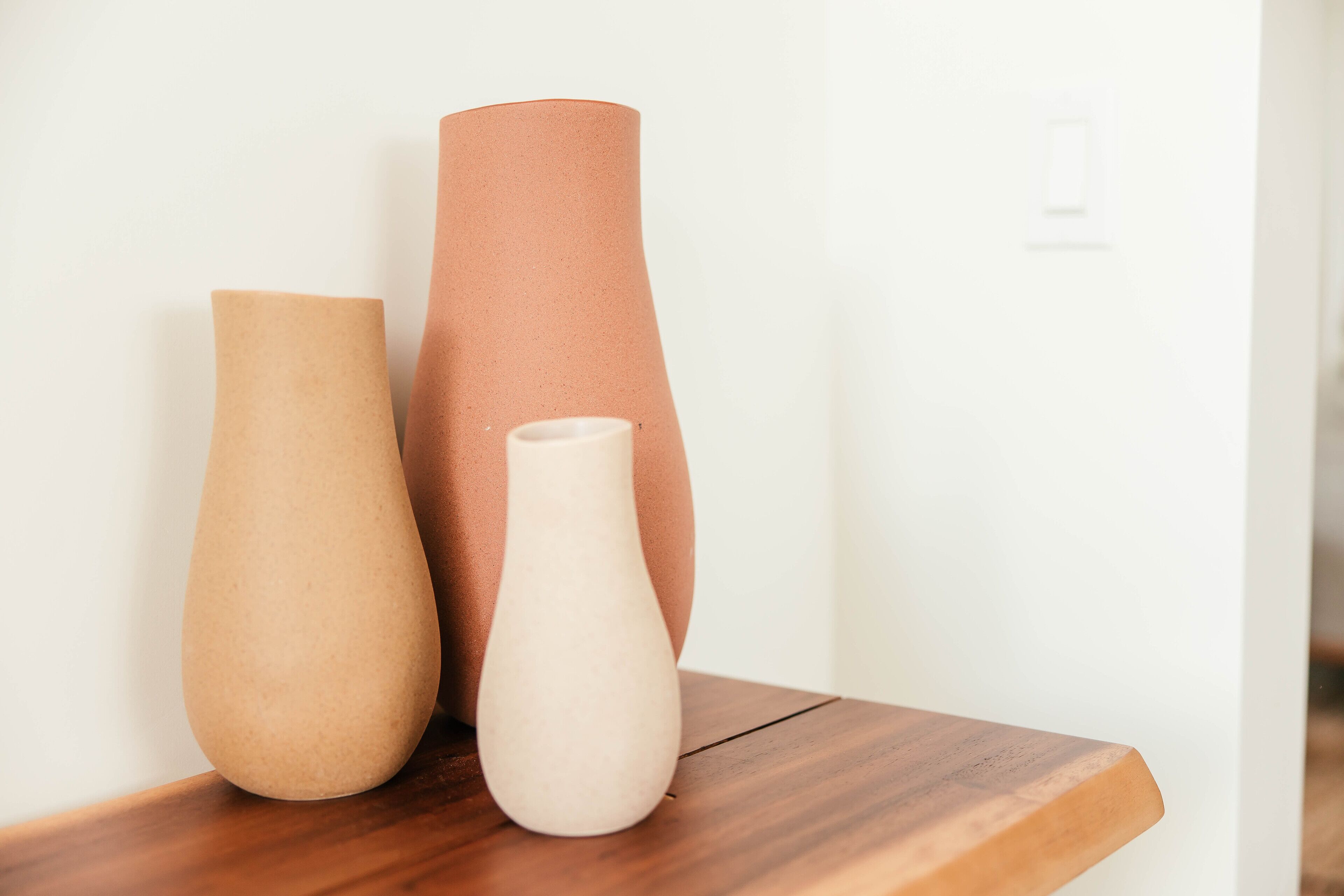 Trois vases de différentes tailles sont posés sur une étagère en bois, devant un mur blanc.