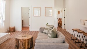 A modern living room with a sofa, wooden coffee table, and a small wooden stool. There are framed pictures on the wall and a basket on the floor. - Luxury Village Home Close to Beaches and Wineries! (Arroyo Grande)