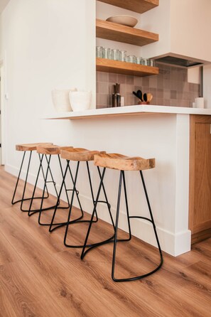 Una cucina con sgabelli di legno, un piano di lavoro bianco e un backsplash piastrellato.