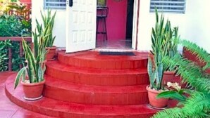 Una entrada de edificio con una escalera roja que lleva a una puerta. Hay plantas en macetas a ambos lados de los escalones.
