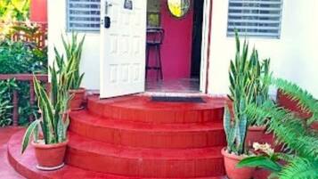A building entrance with a red staircase leading up to a door. There are potted plants on either side of the steps.