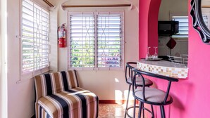 Una habitación pequeña y de colores vivos, con un sofá a rayas, una zona de bar con taburetes y una cocina visible a través de un arco.