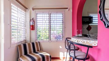 A small, brightly colored room with a striped sofa, a bar area with stools, and a kitchen visible through an archway.