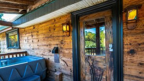 Una cabaña de madera con puerta de cristal, un banco y un jacuzzi.