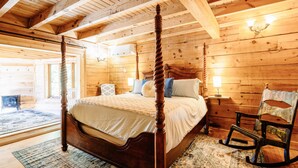 Una cama con dosel en un dormitorio de cabaña de troncos, con una mecedora y una mesita de noche.