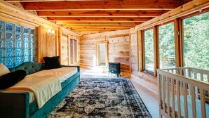 Interior de una cabaña de troncos con cama, cuna, chimenea y ventanas amplias.