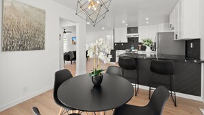 A modern kitchen with black cabinetry, a central island, and a dining area with a black table and chairs. - Safari Vines Retreat. Fully remodeled spacious 3 bedroom 2 bath home   
Sleeps 8 (Escondido)