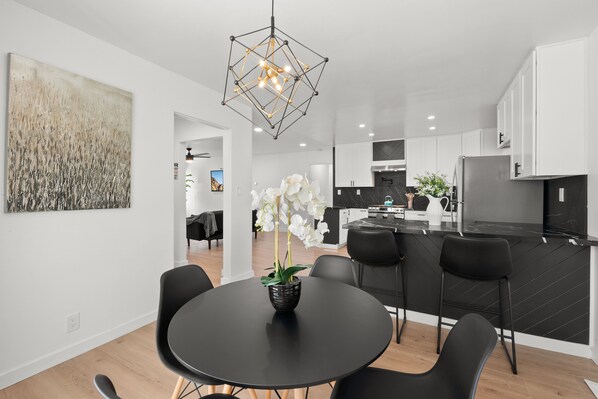 Une cuisine moderne avec des meubles de couleur noire, un îlot central et un coin repas comprenant une table et des chaises noires.