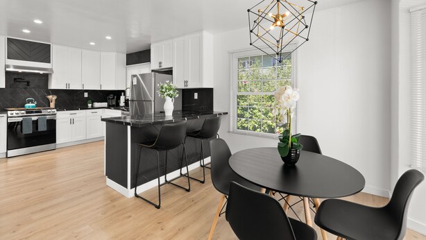 A modern kitchen with white cabinets, a black island, and a dining area with a round table and black chairs. - Safari Vines Retreat. Fully remodeled spacious 3 bedroom 2 bath home   
Sleeps 8 (Escondido)
