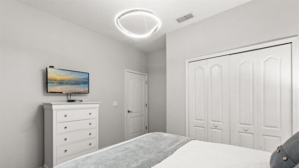 A bedroom with a bed, a dresser, a painting, and a closet. - Comfortable 5BR at Paradise Palms Resort (Kissimmee)