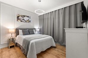 Une chambre à coucher moderne avec un lit, des tables de chevet, un tableau et un téléviseur.