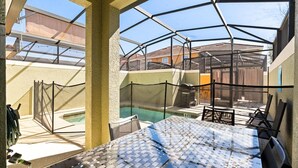 A sunroom with a view of a swimming pool, a patio area with chairs, and a covered outdoor space. - Comfortable 5BR at Paradise Palms Resort (Kissimmee)