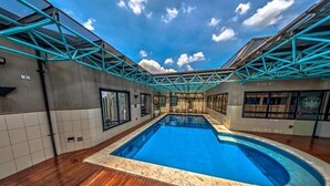 A swimming pool with a wooden deck, surrounded by walls with windows and a metal truss structure. - Flat Massis 133 - Bela Vista (São Paulo)