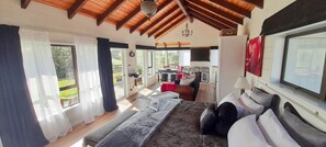Ein großzügiger Wohnbereich mit einem großen Bett, einer Couch und einem Esstisch. Eine Küchenzeile mit Herd und Kühlschrank ist ebenfalls vorhanden. Das Zimmer verfügt über große Fenster und eine Holzbalkendecke.