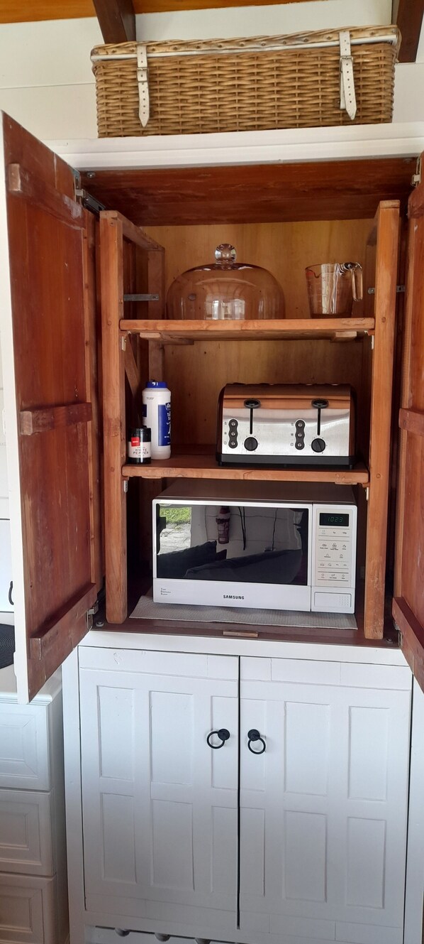 A wooden cabinet with a microwave, a kettle, and a basket on top.