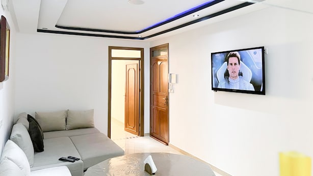 Un soggiorno moderno con un divano, una televisione a parete e una porta in legno che dà su un'altra stanza.