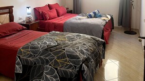 Camera d'albergo con due letti, una lampada da terra, una finestra con tende e un appendiabiti.