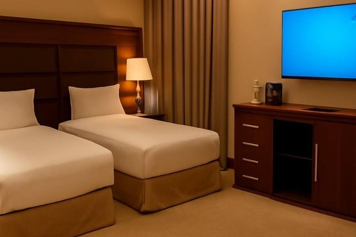A hotel room with two beds, a TV, a lamp, and a wooden cabinet.