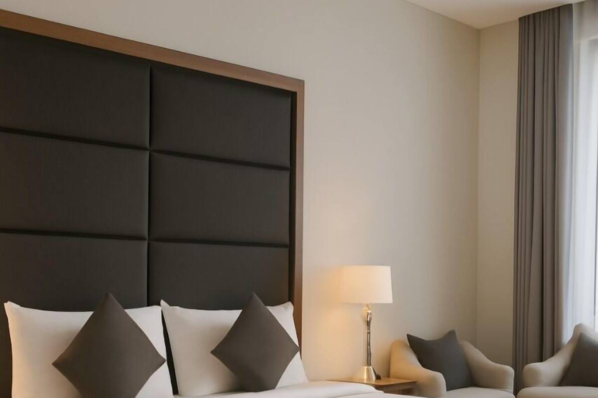 A large bed with a headboard, two bedside tables, a lamp, and two chairs.
