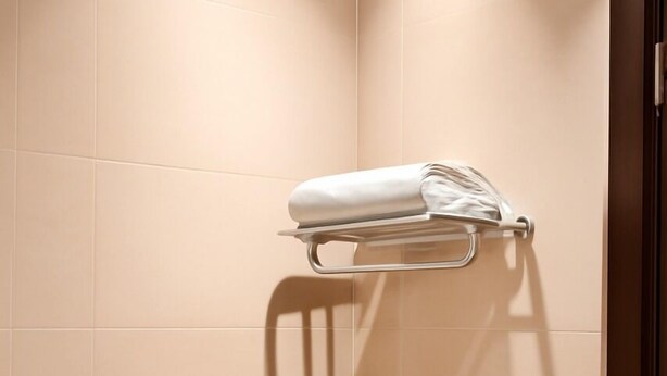 A corner of a room with beige tiled walls and a towel rack holding a folded towel. - Daif Inn Serviced Apartment - Qurtuba (Riyadh)